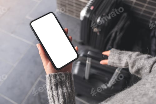 Preview: a woman holding black mobile phone with blank desktop screen while while holding a baggage