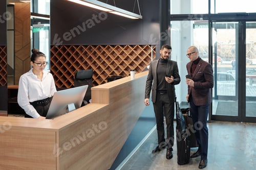 Preview: Businessmen discussing data in smartphone while receptionist using computer