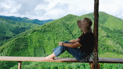 Preview: Rear view of a woman sitting on wooden terrace and looking at a mountain view