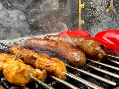 Preview: BBQ food sizzling on a smokey grill, sausages, chicken satay and red bell pepper barbecue cooking.