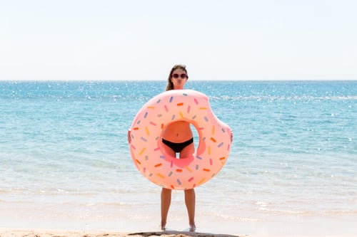 Preview: happy female on the beach playing with an inflatable donut ring. Summer holidays