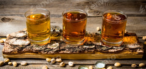 Preview: Three beers on birch stand with pistachios around.