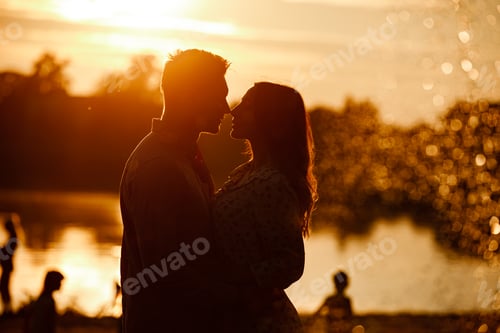 Preview: silhouette of loving couple hugging on the lake at sunset. Beautiful young couple in love walking
