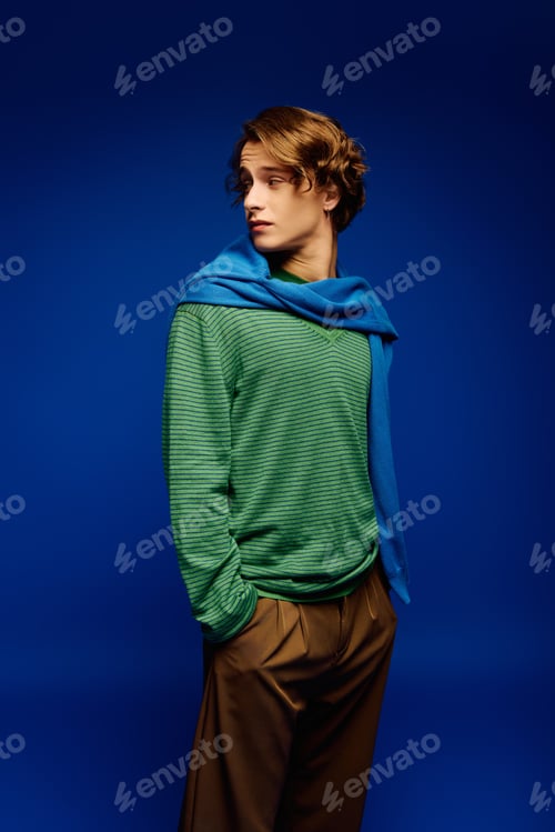 Preview: Stylish young man showcases modern fashion in vibrant blue backdrop with confidence and charm