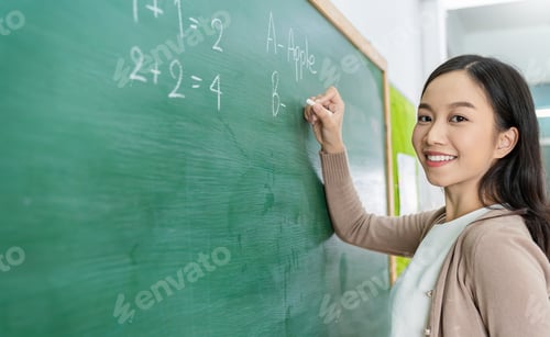 Preview: Closeup portrait of young happy asian teacher write on chalk board.