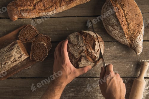 Preview: partial top view of person cutting loaf of bread with knife