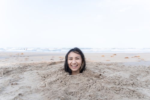 Preview: A young Hispanic woman is having fun while buried in the sand of the beach
