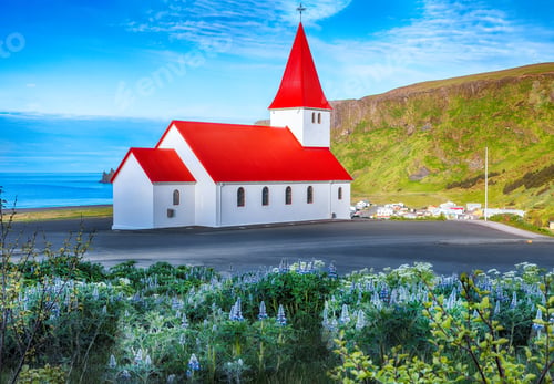 Preview: Impressive view of Vikurkirkja christian church in blooming lupine flowers.