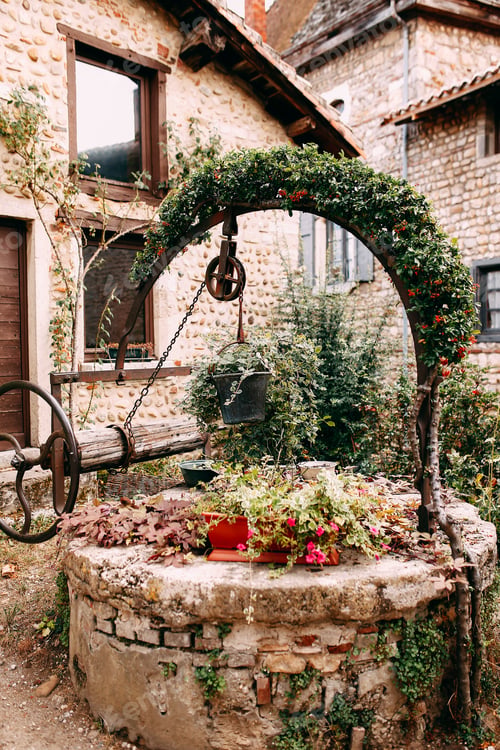 Preview: Old wooden stone well with red flower arch and ivy in Perouges, France
