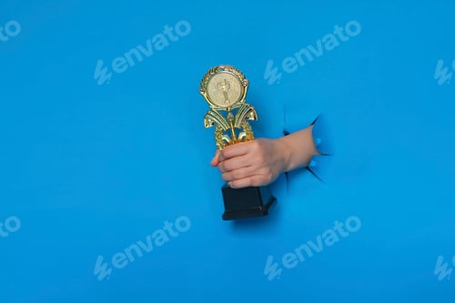 Preview: image of trophy in hand, concept for winning or success. Golden trophy on blue background, top view