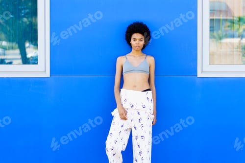 Preview: Young black woman with afro hair, fashion model, posing against an urban blue wall