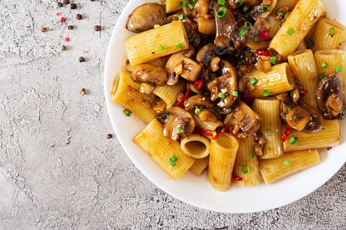 Preview: Vegetarian pasta rigatoni with mushrooms and chilli peppers in white bowl on grey table.