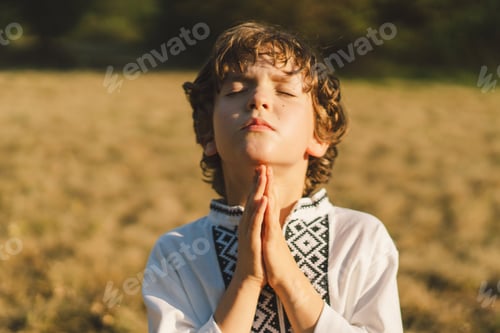 Preview: A young child wearing a traditional embroidered shirt quietly prays outdoors