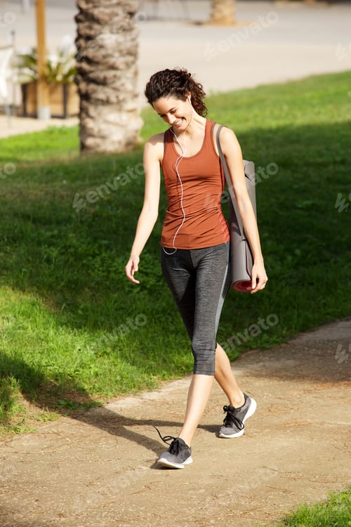 Preview: happy young woman walking to yoga lesson in park
