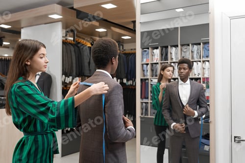 Preview: Man in suit looking at mirror of shop measuring with tape