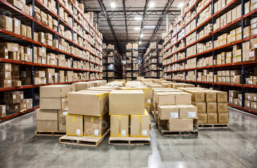 Preview: View down aisles of racks holding cardboard boxes of product on pallets in a large distribution