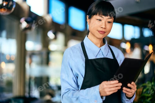 Preview: An Asian waitress holding a bill case and reading a receipt.