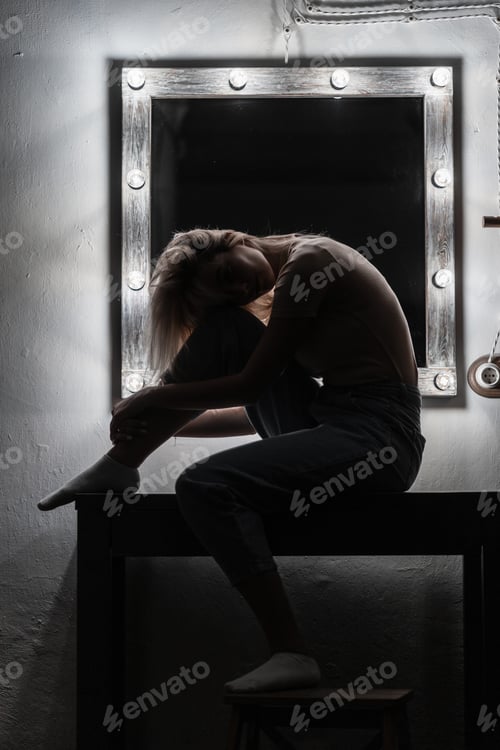 Preview: Pretty fashionable young woman in a blonde in a stylish T-shirt in jeans sits near a mirror