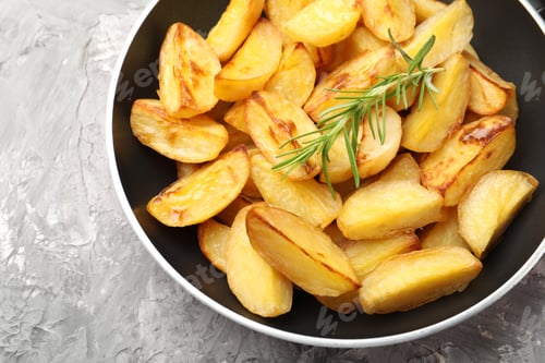 Preview: Tasty baked potatoes with rosemary in frying pan on grey textured table, top view