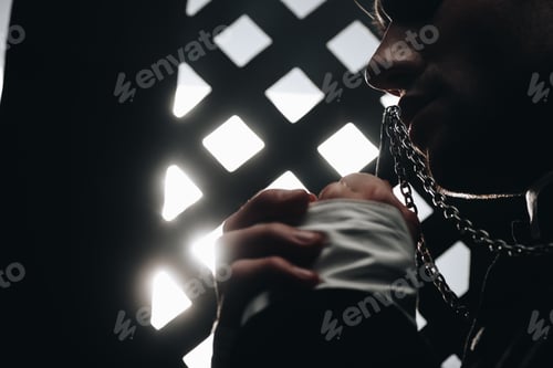 Preview: cropped view of catholic priest kissing cross on his necklace near confessional grille in dark with