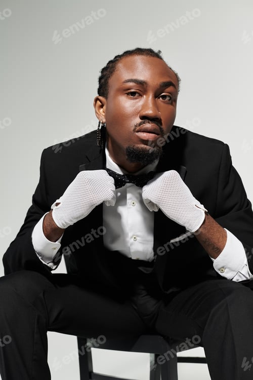 Preview: Confident young African American man in a suit showcasing elegance against a grey backdrop