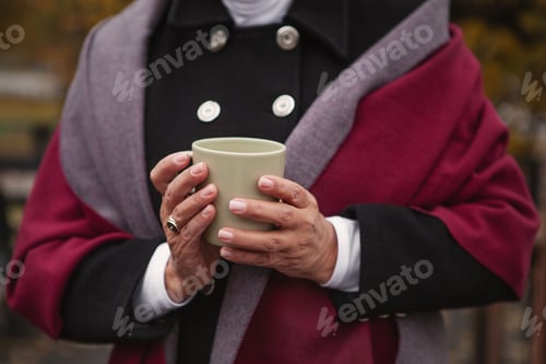 Preview: Close up hands of senior woman, cozy dressed warm clothes, holding cup with coffee or tea