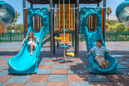 Preview: Schoolchild playing in a playground together sliding a slide