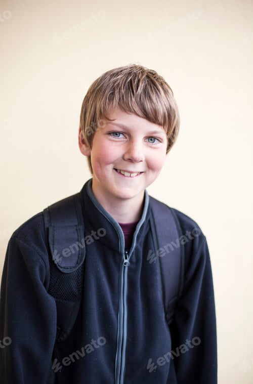 Preview: Portrait of happy junior high schoolboy standing against wall