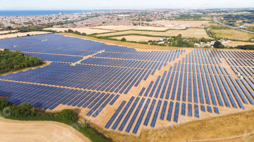 Preview: Drone shot of The Solar Panel Farm with sea and city in the background in UK