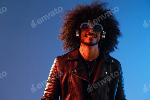 Preview: Portrait of a stylish man with curly hair with glasses and headphones on a blue background