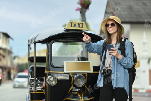 Preview: Happy caucasian female traveller with backpack using smart phone front of Tuk Tuk taxi in Chiang Mai