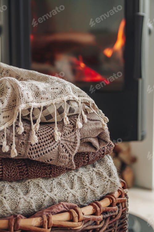 Preview: A stack of warm clothes in a wicker basket an iron fireplace wit