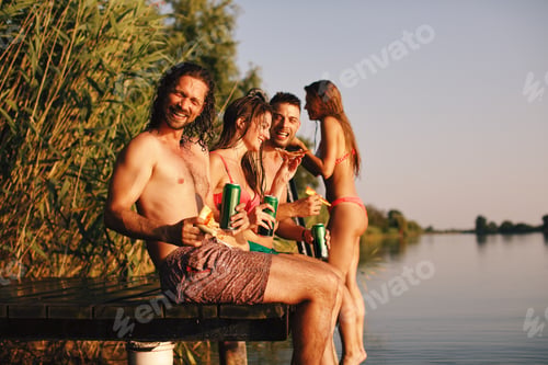 Preview: Group of young people eats pizza and drinking beer on a dock by the river