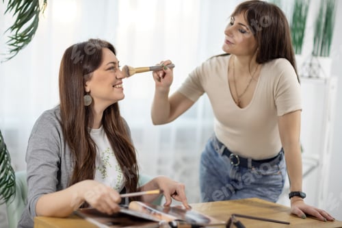 Preview: Two girlfriends in stylish clothes make each other make-up near the table with a magazine