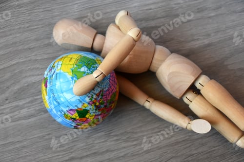 Preview: Tired wooden human figure lying on the floor and holding globe planet Earth. World Financial crisis