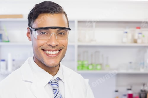 Preview: Smiling male scientist in safety goggles, lab coat, striped tie posing in lab with green solution