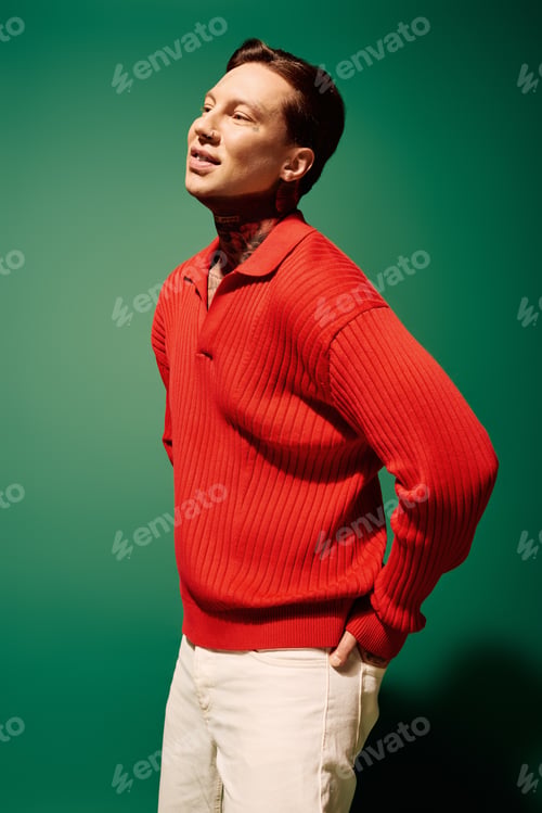 Preview: A young man with tattoos poses confidently in a vibrant red sweater against a green backdrop