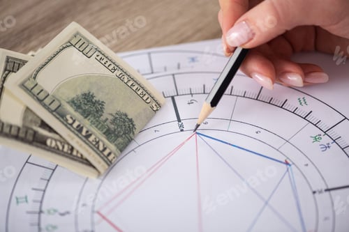 Preview: Cropped view of astrologer drawing natal chart beside dollar banknotes on table