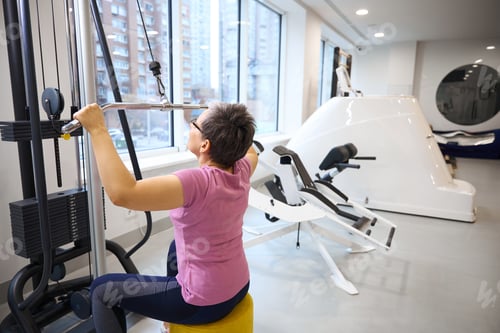 Preview: Mature woman wearing sportswear doing sport exercise for back in gym