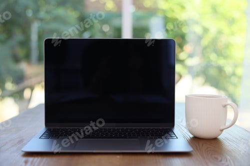Preview: Open laptop and cup on wooden table against blurred green background, closeup. Mockup for design