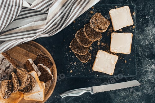 Preview: top view of fresh toasts with butter and healthy multigrain bread with knife on black