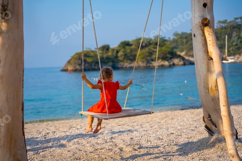 Preview: Little girl on wooden swing on Oludeniz beach. Summer holiday in Oludeniz, Turkey. Girl ride on a