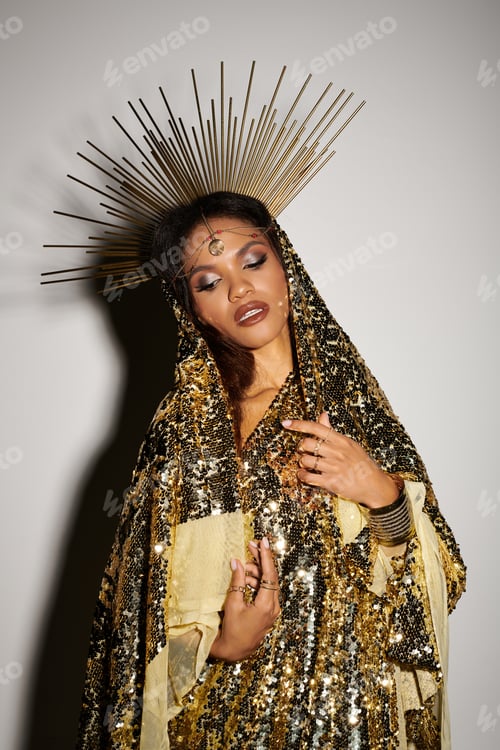 Preview: Gorgeous Black goddess in a shiny gold dress poses in a bright studio at golden hour