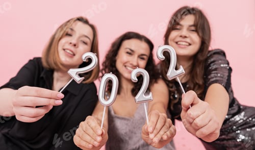 Visualização: Um grupo de garotas está segurando velas dos números 2022 em um fundo rosa.