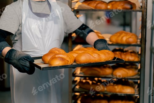 Preview: close up In a professional kitchen an inclusive baker stands with ready-made bread on a tray smiling