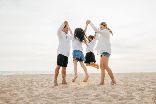Preview: Beachside jubilation as an Asian family with father and mother holding children jumps into air.