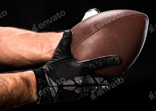 Preview: Close-up view of hands of football player holding rugby ball on black