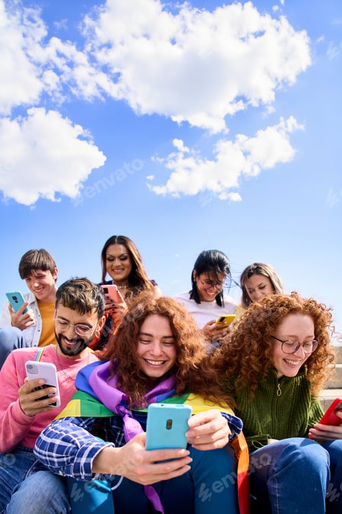 Preview: Smiling young friends using mobile phone celebrating gay pride day together outdoors. Copy space.