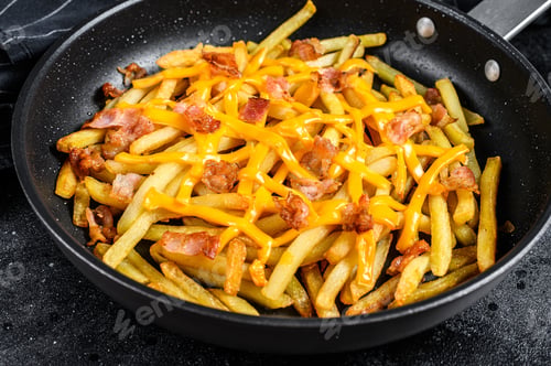 Preview: Golden French fries fried with cheddar cheese and bacon in a pan. Black background. Top view
