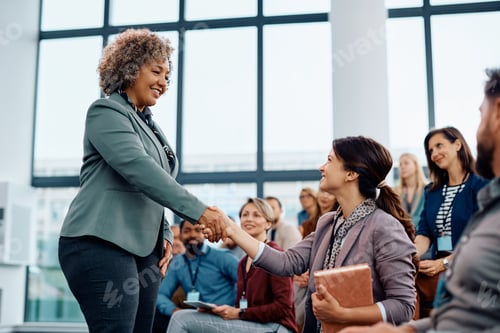 Preview: Happy female entrepreneurs shaking hands while greeting during business seminar in conference hall.